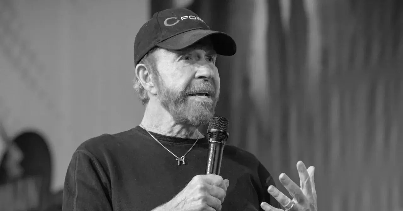 Chuck Norris, mimo swojego wieku, wciąż ma charyzmę. Mówi do mikrofonu w czapce z daszkiem.