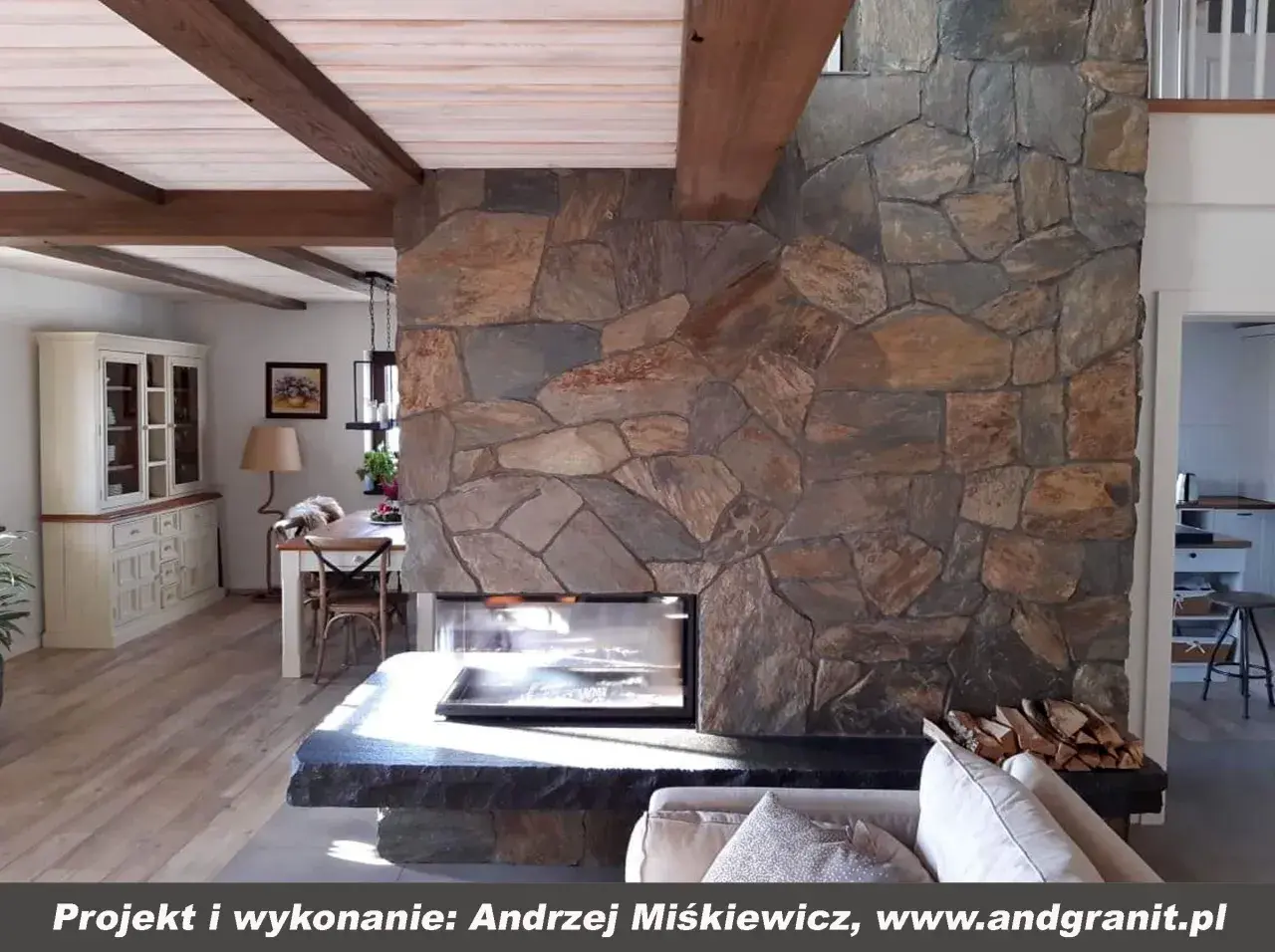 Kamienny kominek z naturalnego łupku, z drewnianymi belkami na suficie, tworzy przytulną atmosferę w salonie.