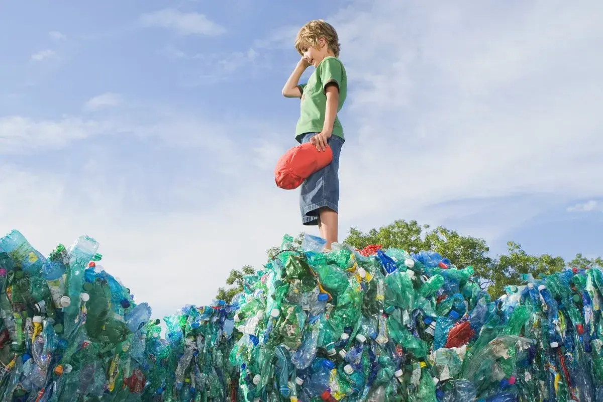 Chłopiec stoi na górze sterty plastikowych butelek, zastanawiając się, co to za pla.