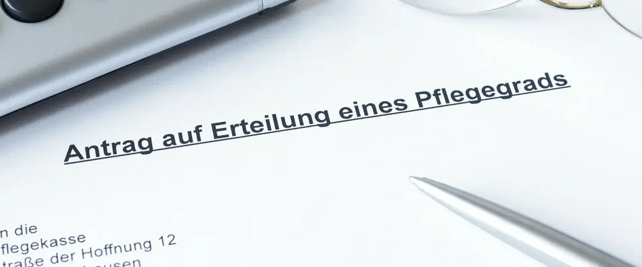 Ein Dokument mit der Überschrift "Antrag auf Erteilung eines Pflegegrads" liegt auf einem Tisch. Daneben liegen ein Stift und eine Brille.