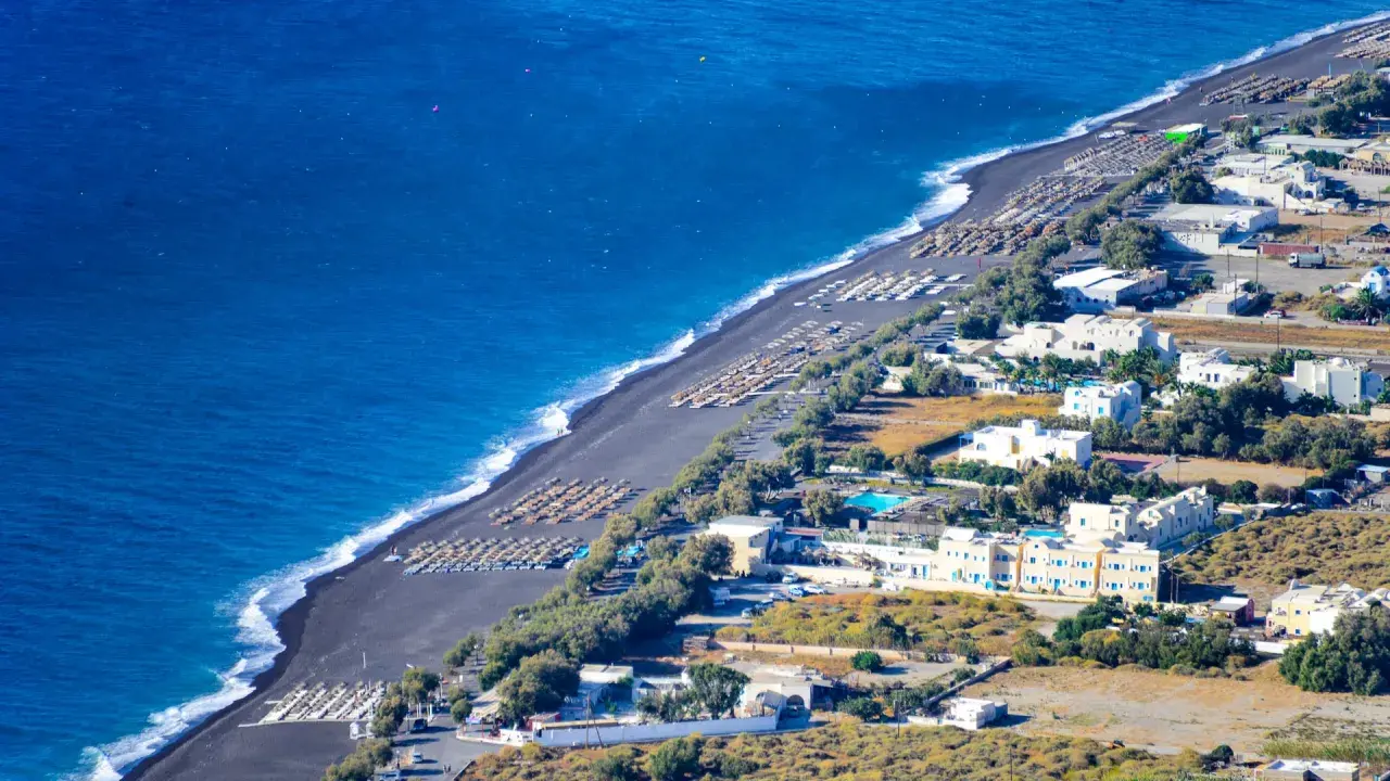 Santorini plaże z czarnym piaskiem, rzędy leżaków i białe budynki hotelowe nad turkusowym morzem.