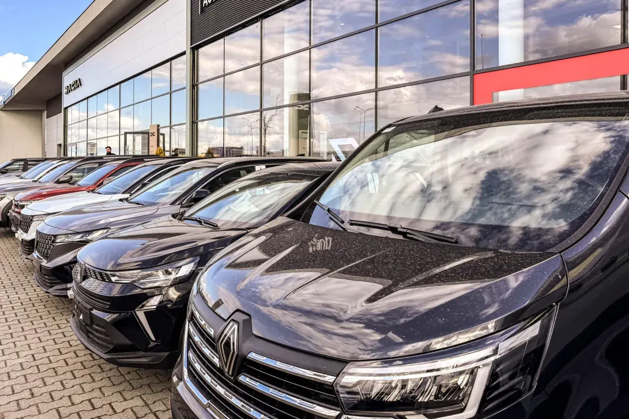 Rząd nowych samochodów na placu. W tle budynek salonu Dacia. Sprawdź autoplac opinie przed zakupem.
