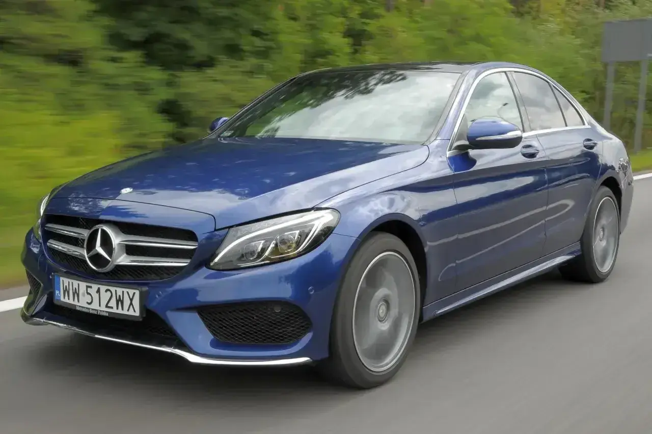 Błękitny Mercedes E220d w ruchu, z rozmytym tłem zieleni i drogi. Elegancki sedan na polskich tablicach rejestracyjnych.