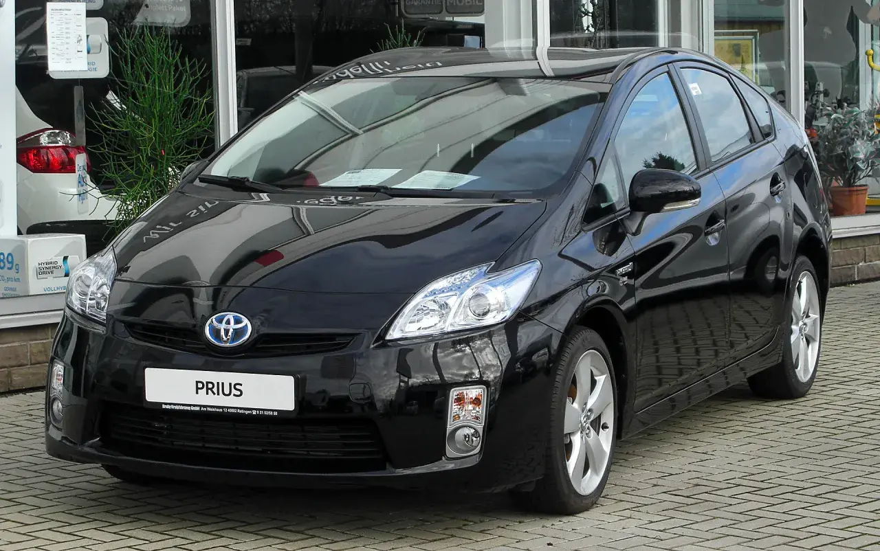 Czarny Toyota Prius 3, hybrydowy samochód, lśni na tle salonu samochodowego.