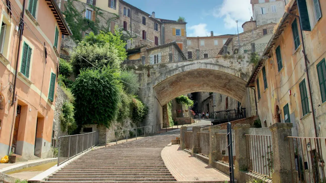 Perugia co zobaczyć: malownicze schody prowadzące pod zabytkowy most, otoczone kamiennymi domami i zielenią.