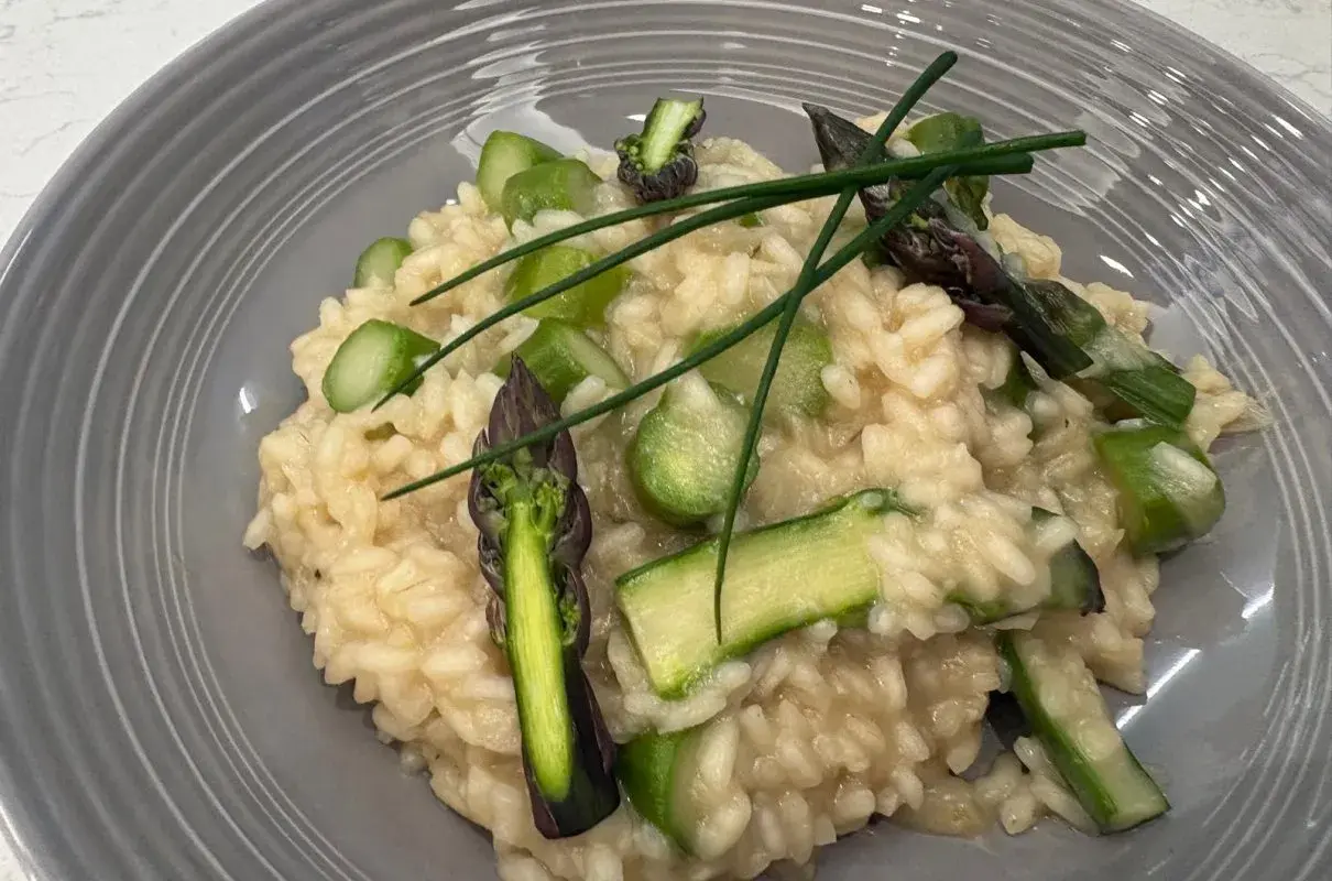 Kremowe risotto z zielonymi szparagami i szczypiorkiem na szarym talerzu.