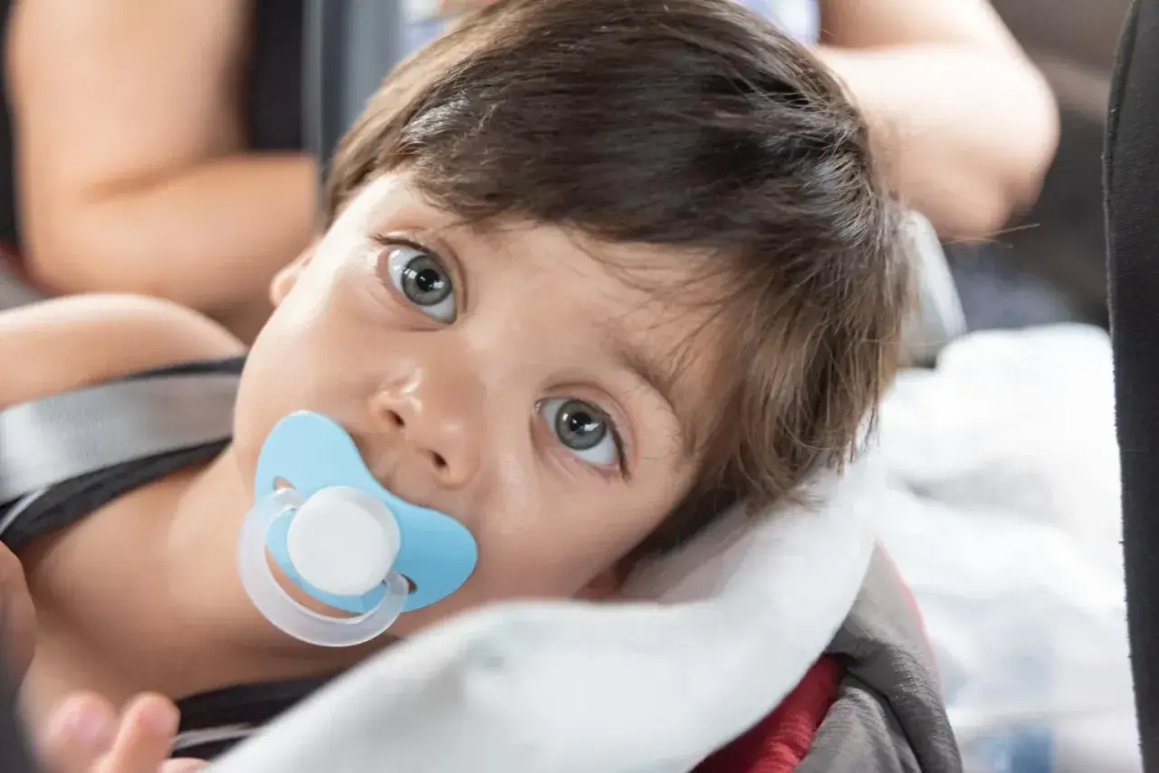 Małe dziecko z niebieskim smoczkiem Tommee Tippee w buzi, zapatrzone w dal.
