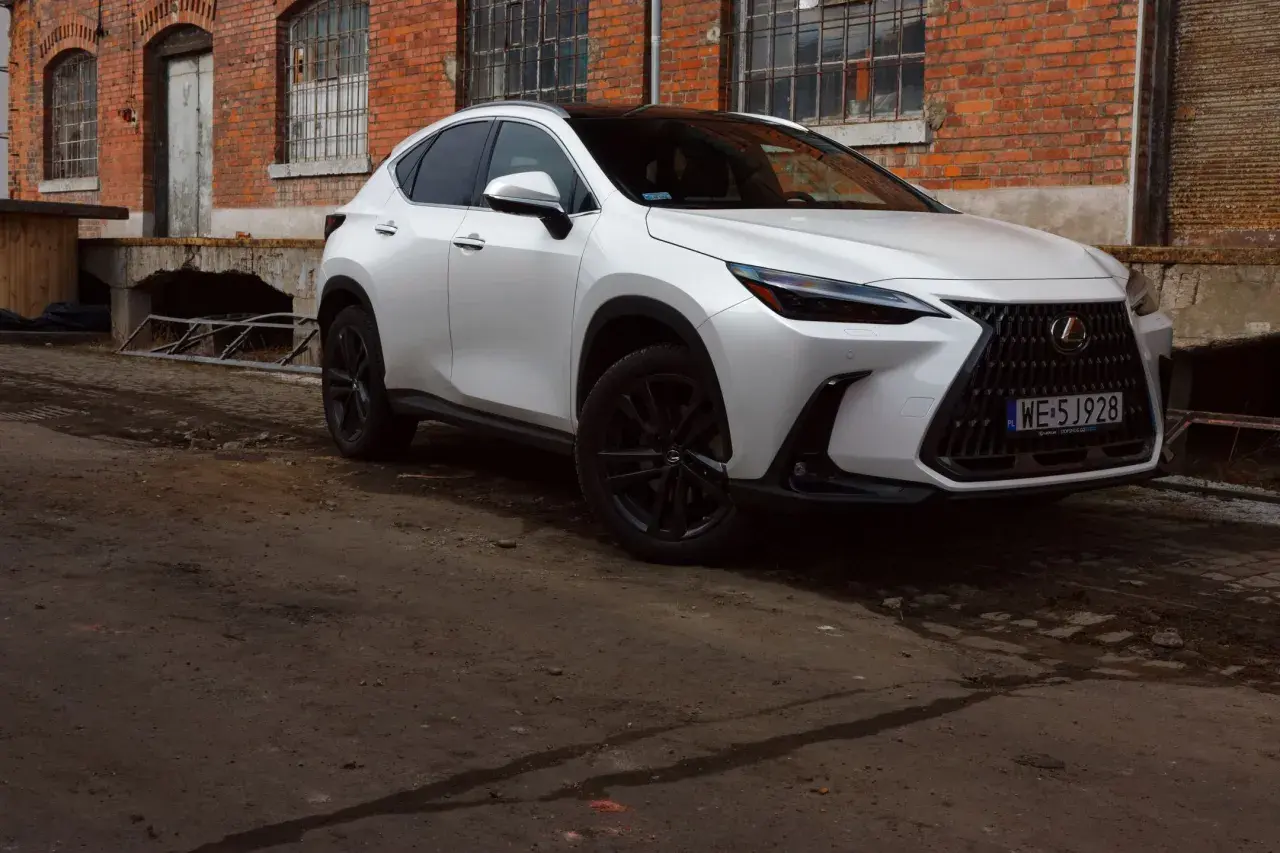 Biały Lexus 350h z czarnymi felgami stoi przed starą ceglaną budowką.