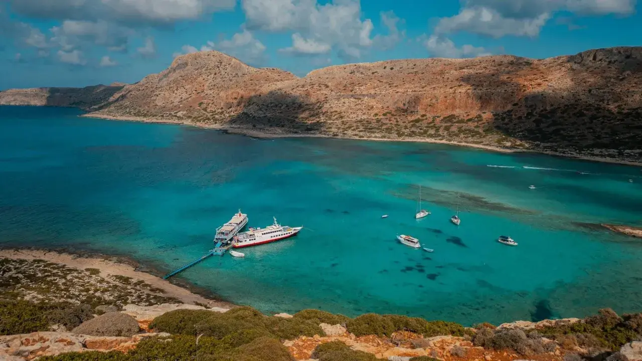 Wycieczka na Santorini z Krety: statki cumują w turkusowej zatoce, otoczonej skalistymi wzgórzami.