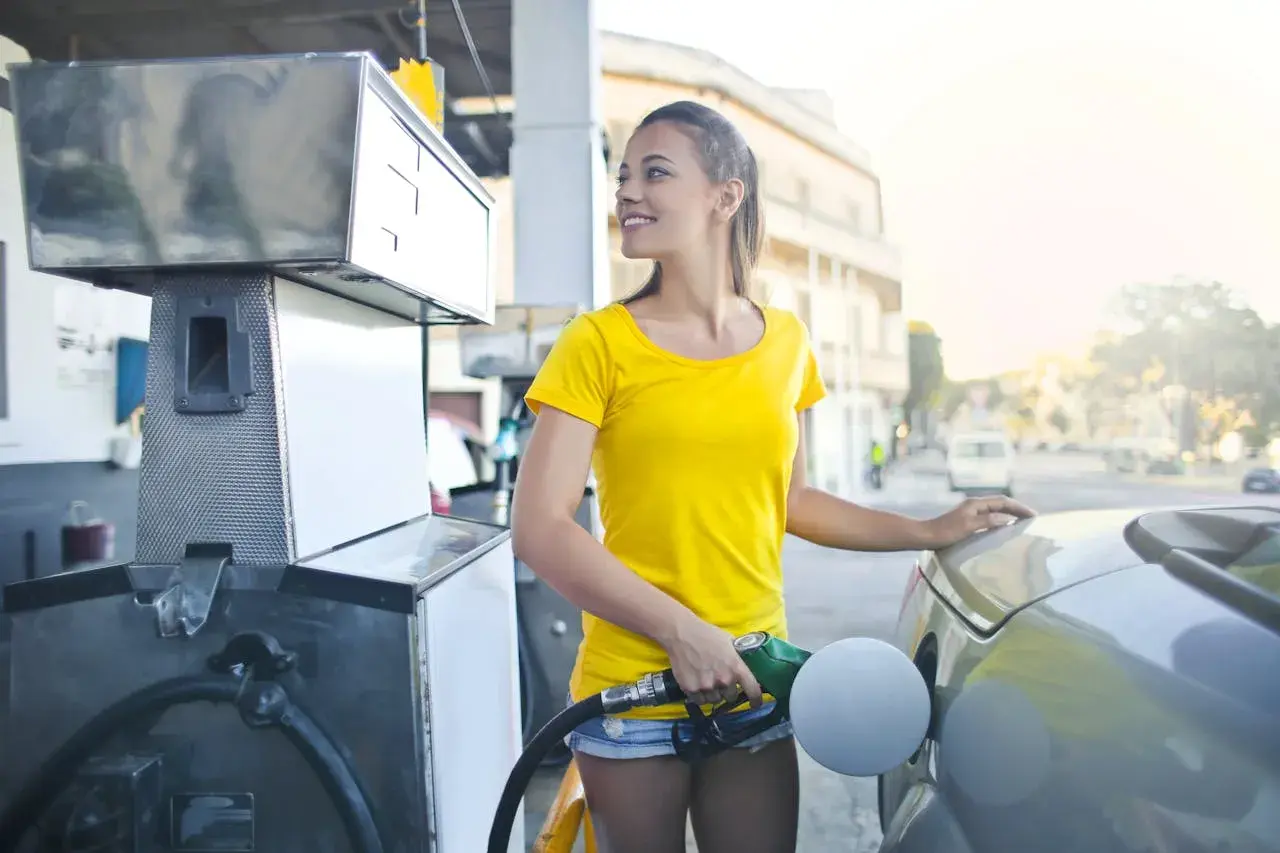 Uśmiechnięta kobieta tankuje auto. Zastanawia się, jak przelać punkty Vitay z karty na kartę, by zaoszczędzić na paliwie.
