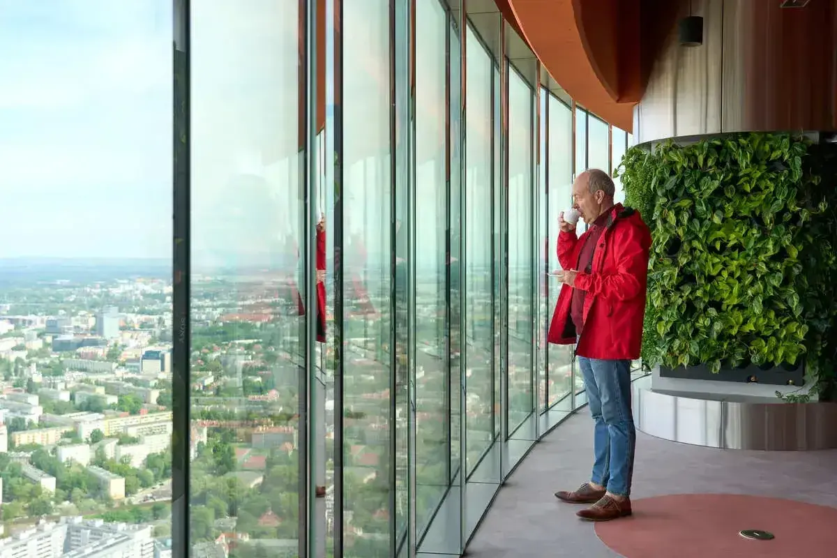 Mężczyzna pije kawę, podziwiając panoramę Wrocławia z tarasu widokowego. Sprawdź Sky Tower Wrocław cennik, by poznać ceny biletów.
