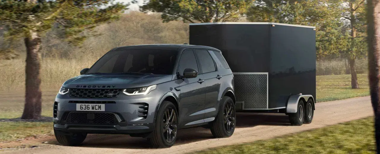 Szary Land Rover Discovery Sport z przyczepą o masie 2000 kg jedzie po leśnej drodze.