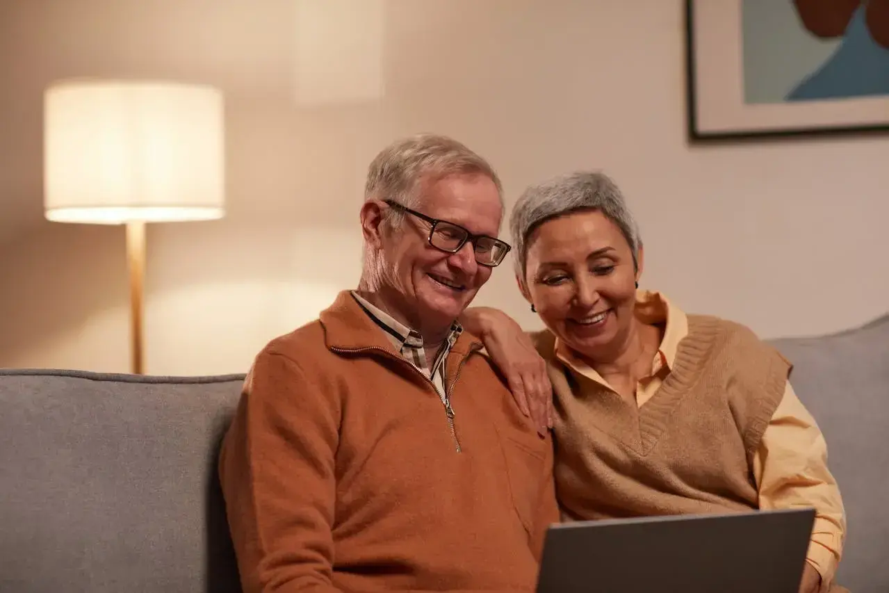 Uśmiechnięta para seniorów przegląda coś na laptopie. Zastanawiają się, czy zwolnienia lekarskie mają wpływ na wysokość emerytury.