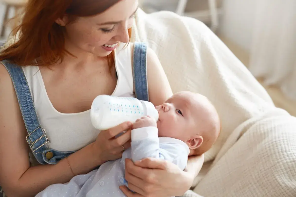 Uśmiechnięta mama karmi piersią swoje dziecko z butelki, szukając najlepszych butelek dla noworodka.