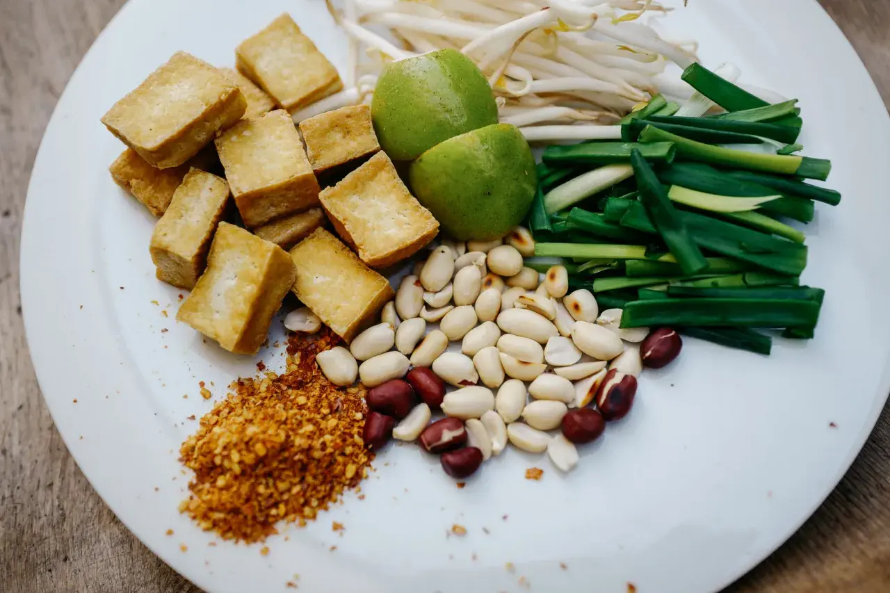 Składniki do pad ka prow: smażone kostki tofu, kiełki fasoli mung, szczypiorek, orzeszki ziemne, limonka i płatki chili.