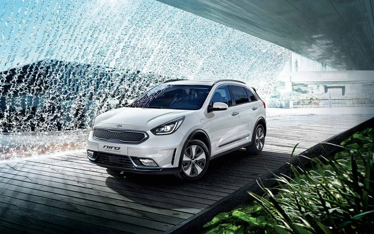 Biały Kia Niro Plug-in Hybrid na drewnianej platformie, otoczony wodnymi kaskadami i zielenią.
