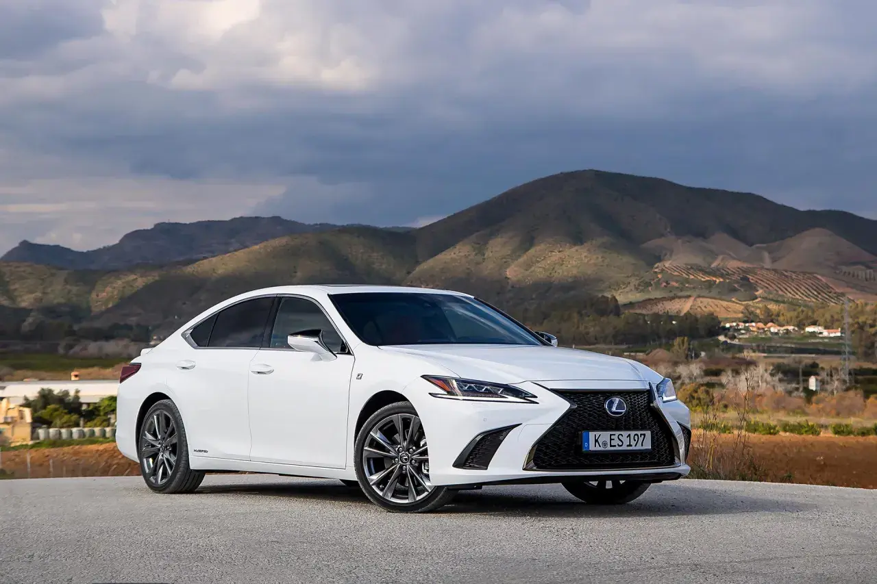 Biały Lexus ES 300h zaparkowany na tle górskiego krajobrazu. Elegancki sedan prezentuje się okazale na tle natury.