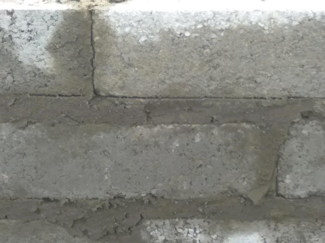 Widok z bliska na ścianę z bloczków betonowych, pokazujący grubość spoiny między nimi.