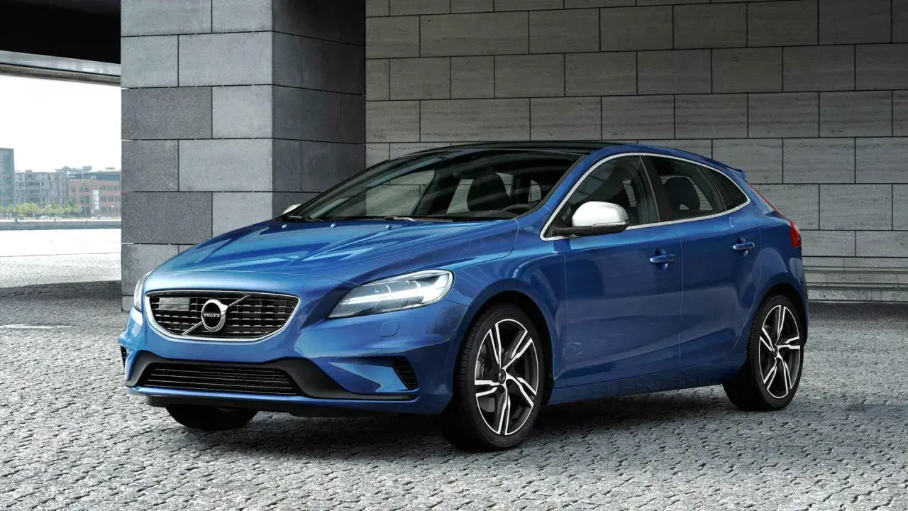Niebieskie Volvo V40 D2 z czarnym dachem, zaparkowane na kamiennej nawierzchni, z nowoczesną architekturą w tle.