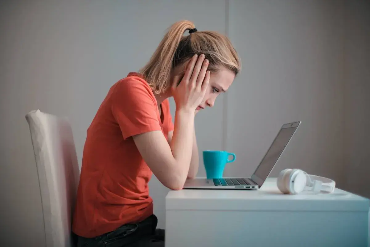 Zmartwiona kobieta przy laptopie, zastanawia się, czy porzucenie pracy wlicza się do emerytury. Na biurku kubek i słuchawki.