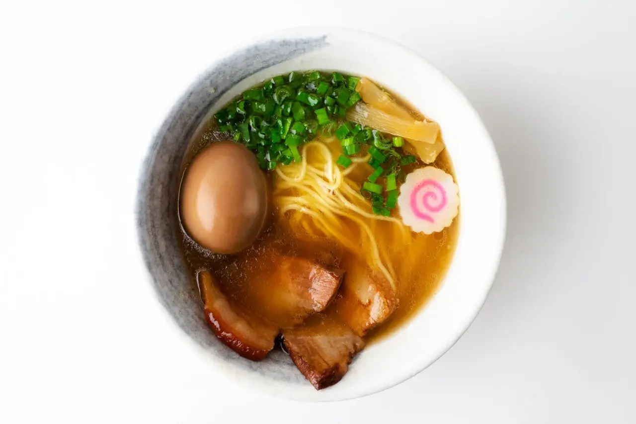A miseczce shoyu ramen z makaronem, jajkiem, plastrami wieprzowiny, szczypiorkiem, bambusem i różową rybną kluską.