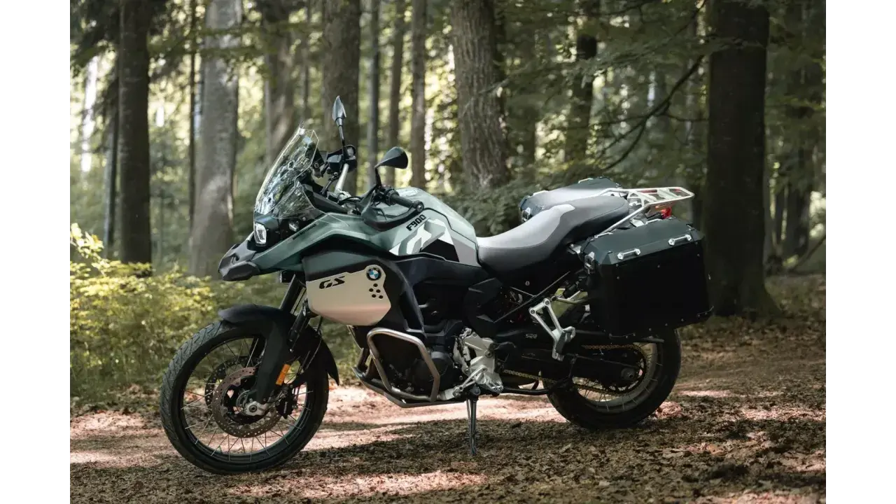 Zielony motocykl BMW F900GS z kuframi, gotowy na przygodę w lesie.