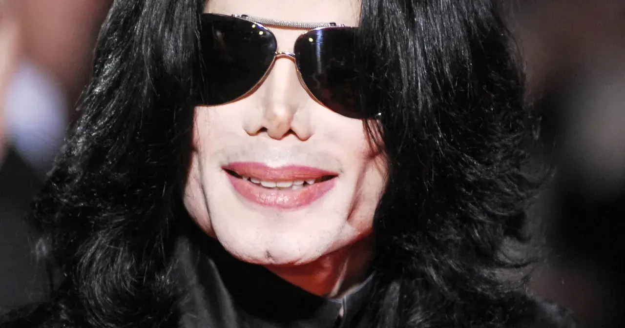 Michael Jackson w okularach przeciwsłonecznych i czarnych włosach. Jego uśmiech i twarz budzą pytania, jak zmarł Michael Jackson.