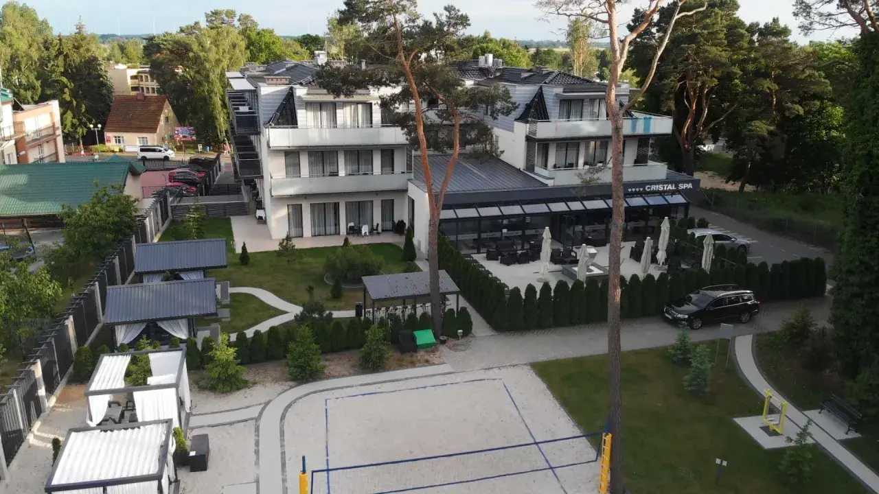 Nowoczesny hotel Cristal Spa z basenem i kortem do siatkówki plażowej, otoczony zielenią.