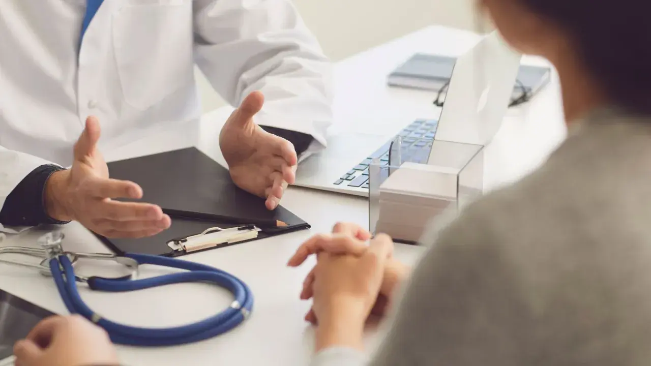 Lekarz omawia z pacjentem diagnozę, być może f43 kod choroby. Na stole stetoskop i laptop.