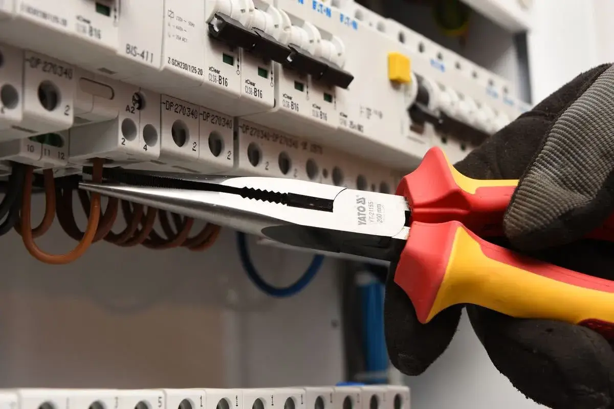 Elektryk w rękawicy wymienia instalację elektryczną, używając kombinerki do przewodów w skrzynce z bezpiecznikami.