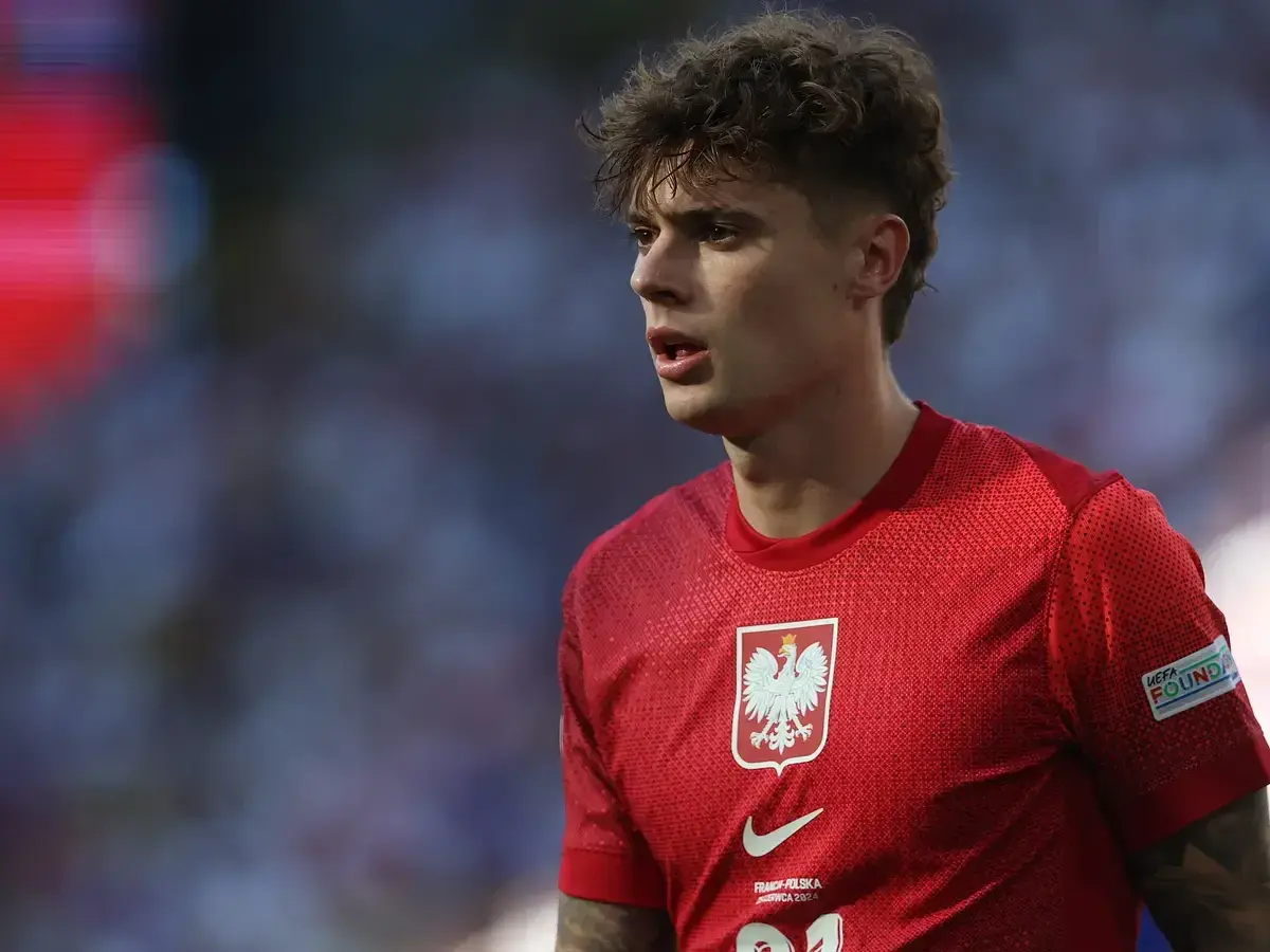 Młody piłkarz w czerwonej koszulce z orłem, symbolizujący polską reprezentację. Jego wzrost i determinacja na boisku budzą nadzieję na przyszłe sukcesy.