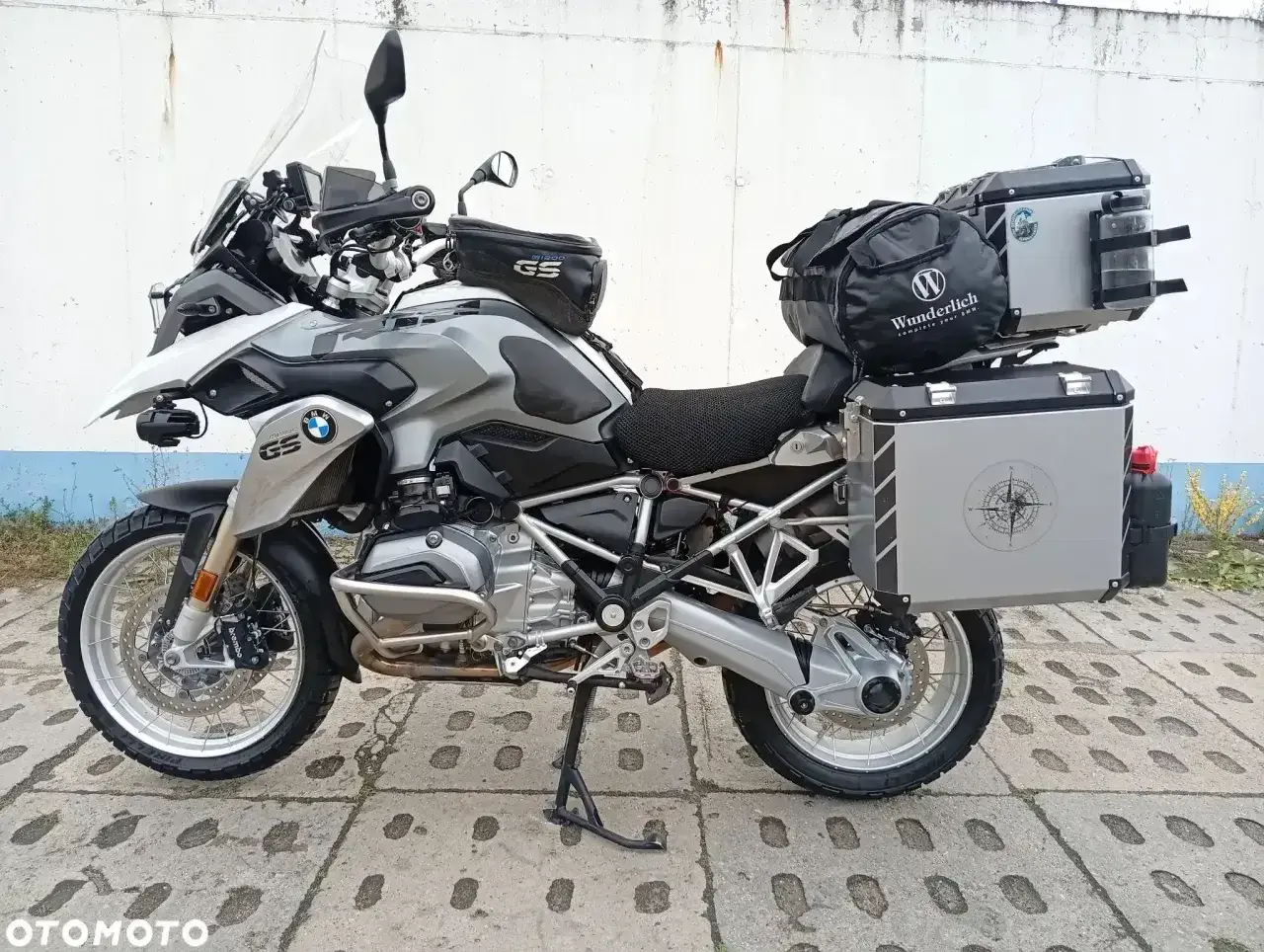 Srebrny motocykl BMW R1200GS z kuframi i torbą na bak. Wady tego modelu to m.in. wysoka cena i skomplikowana elektronika.