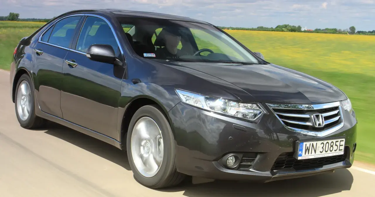 Ciemnoszary sedan Honda Accord, idealny auto do 40 tys., jedzie przez pola rzepaku.