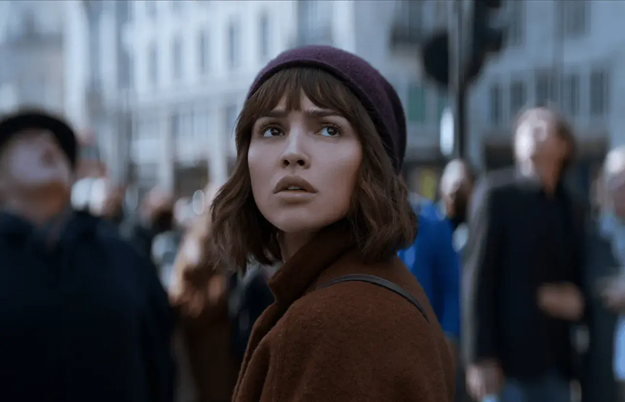 Młoda kobieta w brązowym płaszczu i bordowej czapce patrzy w górę, otoczona tłumem. Czy to zapowiedź netflix nowości dzisiaj?