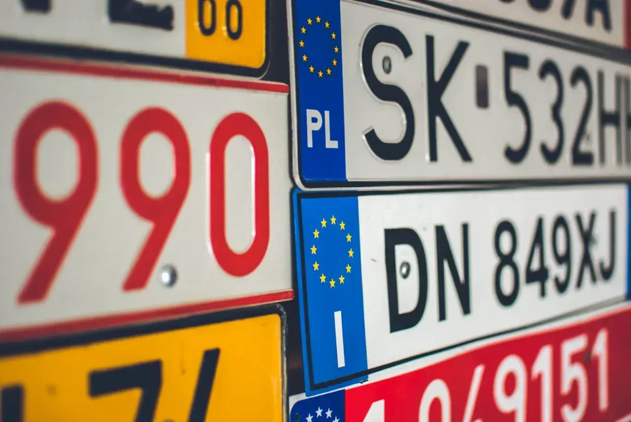Zbliżenie na stos tablic rejestracyjnych z różnymi kody samochodowe. Widoczne numery to m.in. 990, SK 532HH, DN 849XJ.
