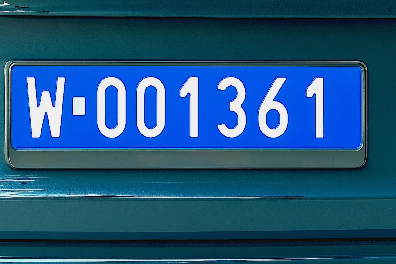 Niebieskie tablice rejestracyjne z numerem W-001361 na ciemnozielonym samochodzie.