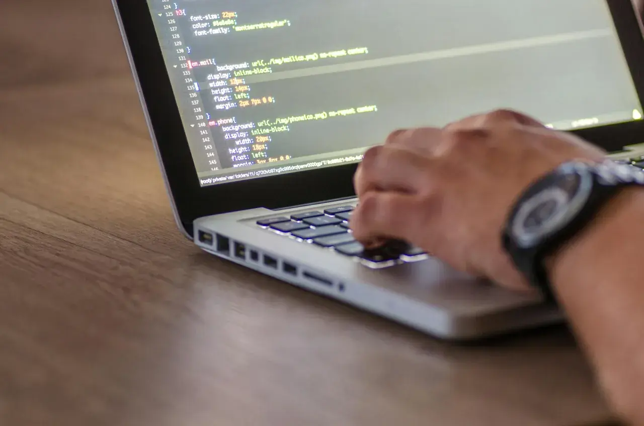 Kodowanie strony internetowej, widać fragment kodu HTML z listą nieuporządkowaną i rękę piszącą na klawiaturze.