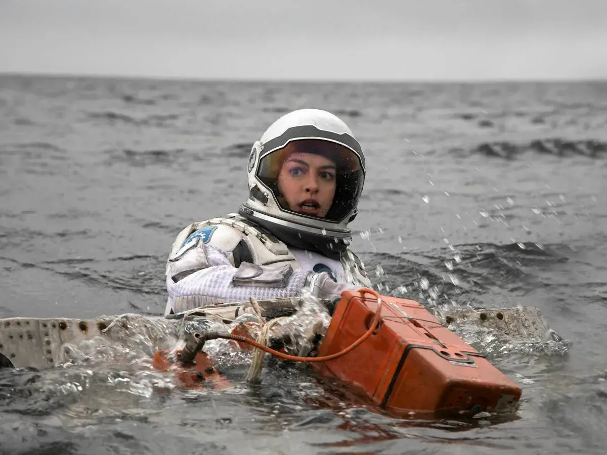 Astronautka w skafandrze z filmu Interstellar 2 w wodzie, z pomarańczowym urządzeniem.