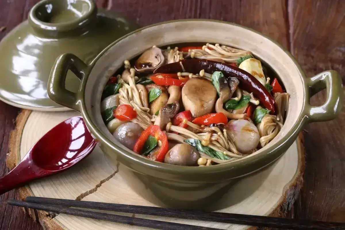 Gęsta zupa z grzybkami mun, enoki, pieczarkami, papryczkami chili i cebulką, podana w glinianym garnku.