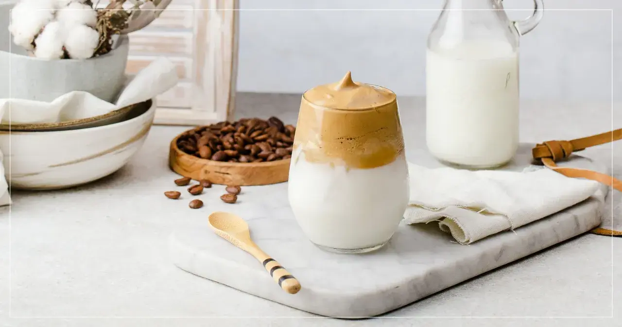 En krämig dalgona coffee med fluffigt skum, serverad med mjölk och kaffebönor.