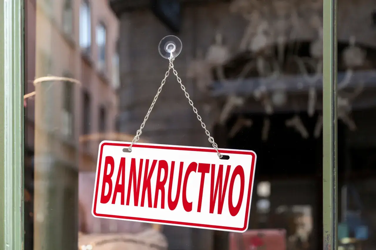 Tabliczka "BANKRUCTWO" wisząca na łańcuszku na szybie.