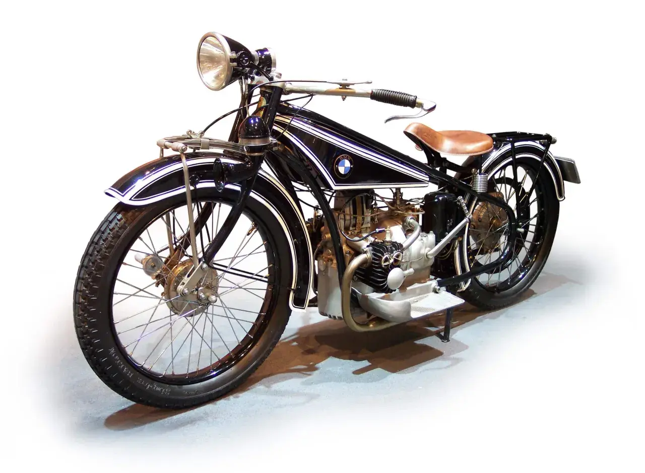 Klasyczny motocykl BMW z lat 20. XX wieku, czarny z białymi pasami, z brązowym siodłem. Ikona historii BMW.