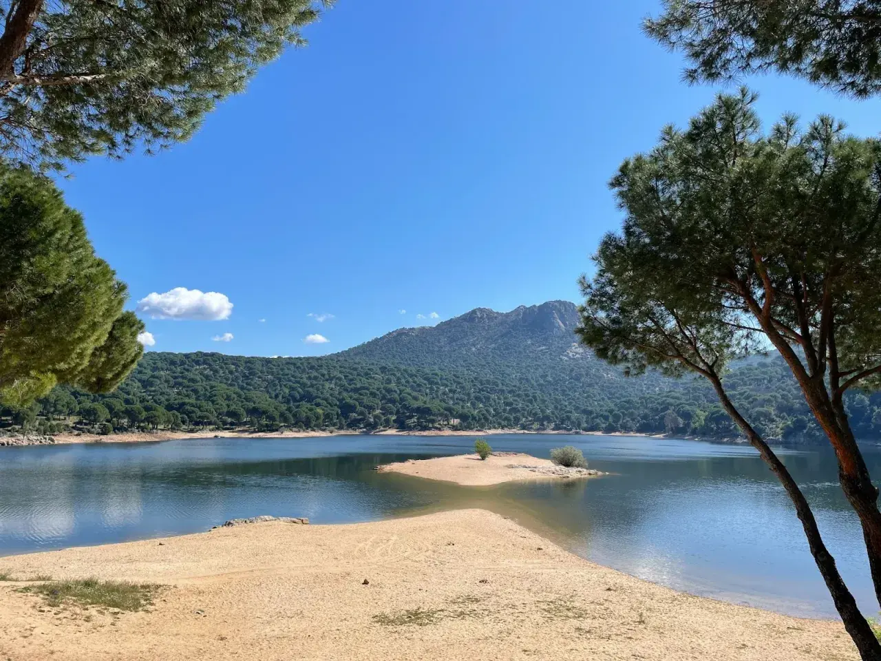 Piękna, piaszczysta plaża nad jeziorem w pobliżu Madrytu, otoczona sosnowym lasem i górami.