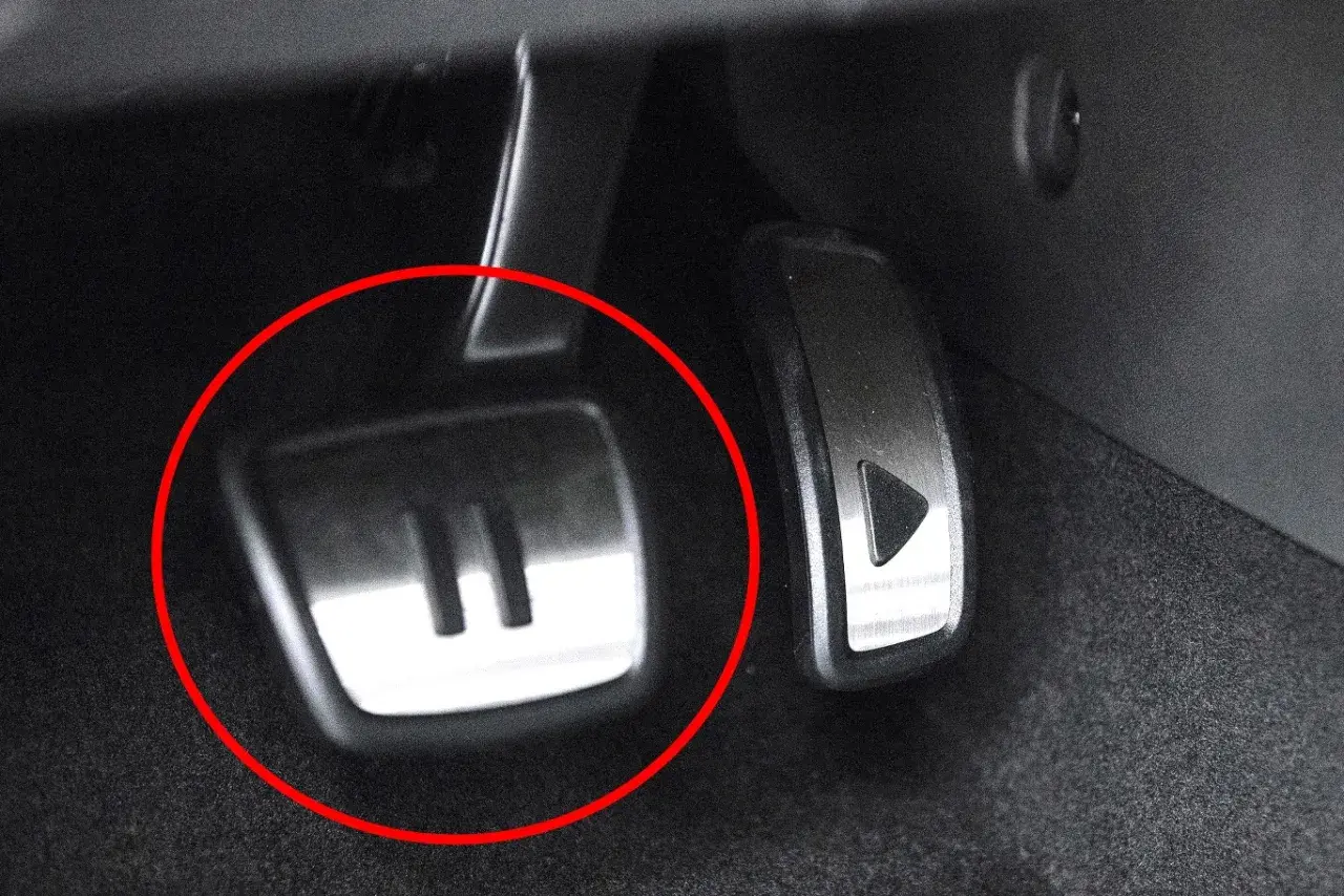 Metalowe pedały w samochodzie, jeden z symbolem "II" (auto hold) i drugi z trójkątem.