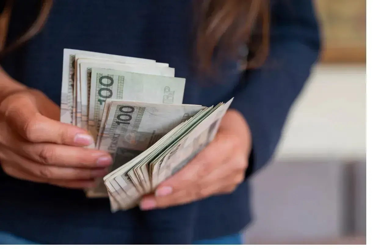 Dłonie trzymające plik polskich banknotów 100 zł. Zastanawiasz się, urlop wychowawczy ile płatny?