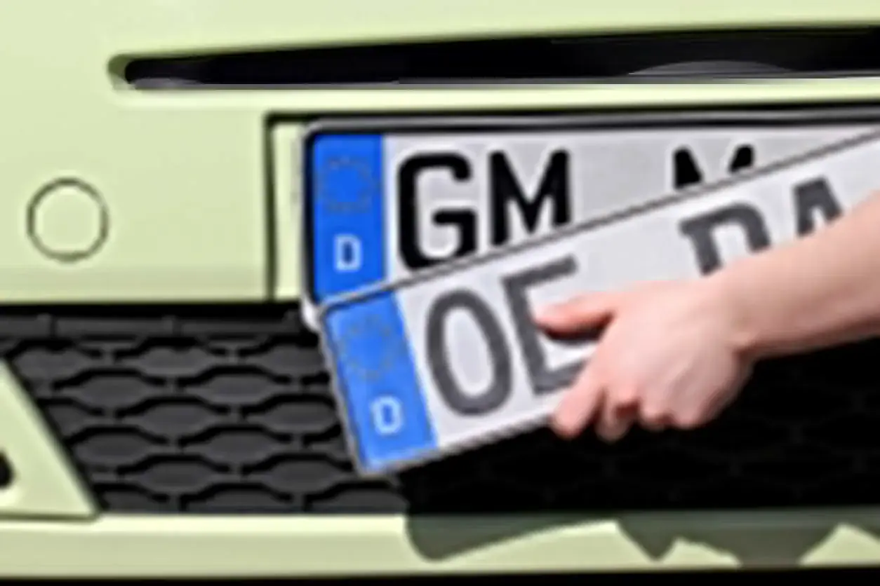 Dłoń trzyma niemieckie tablice rejestracyjne z literami "OE" i "GM".