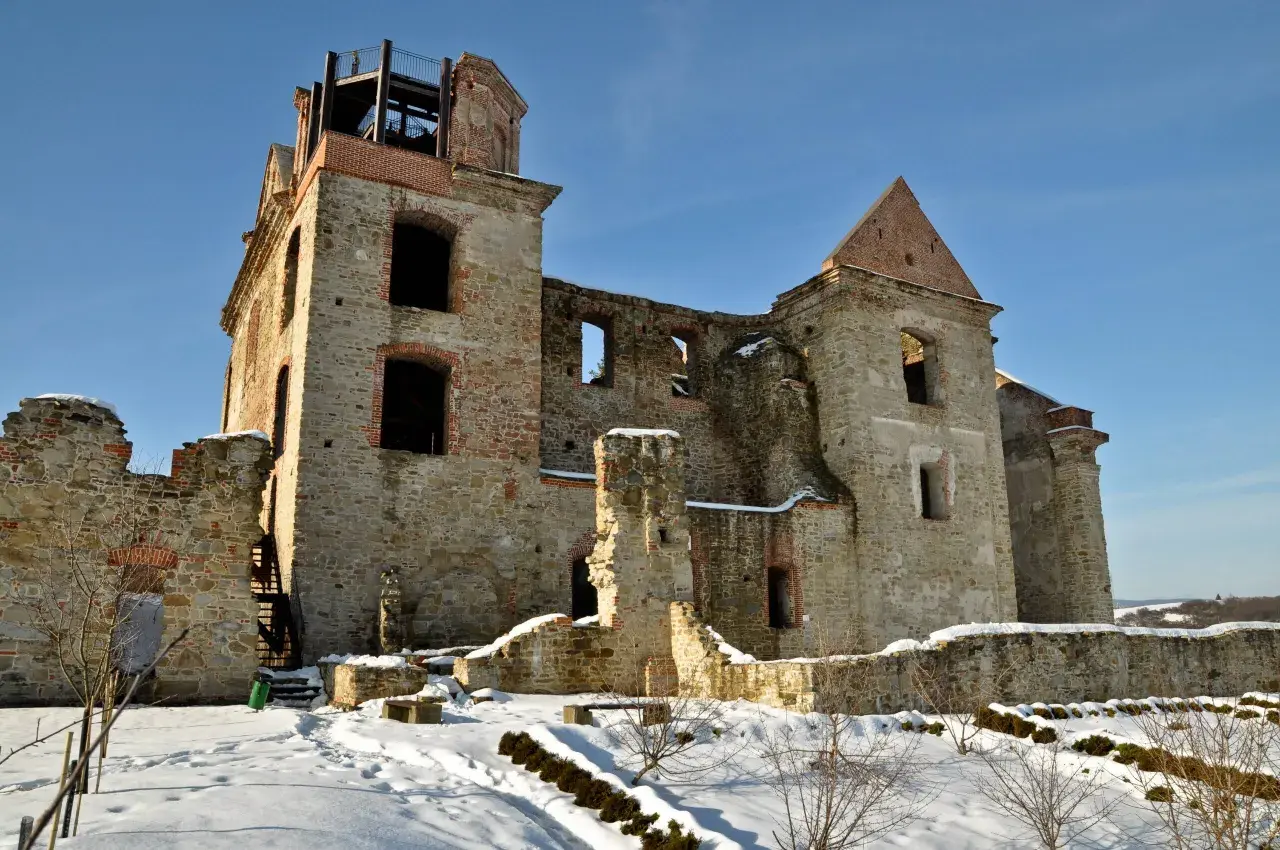 Kamienne ruiny dawnego monastyru w zimowej scenerii. Widać zniszczone mury, łuki okienne i wieżę z platformą widokową.