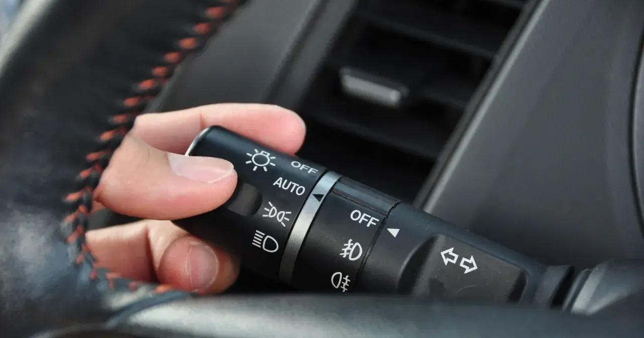 Dłoń ustawia przełącznik świateł w samochodzie, wybierając, na jakich światłach się jeździ: AUTO, OFF, światła mijania lub drogowe.