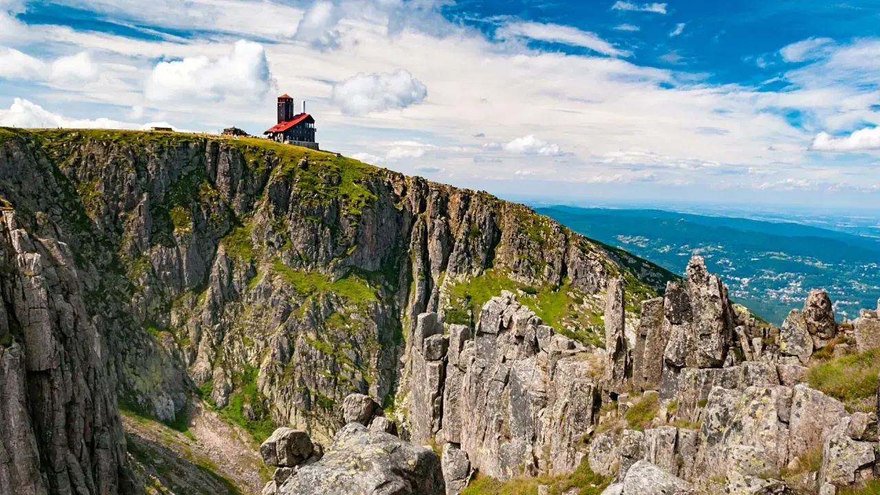 Widok na skaliste zbocze z budynkiem na szczycie. To może być najkrótsza trasa na Śnieżne Kotły, oferująca zapierające dech w piersiach widoki.