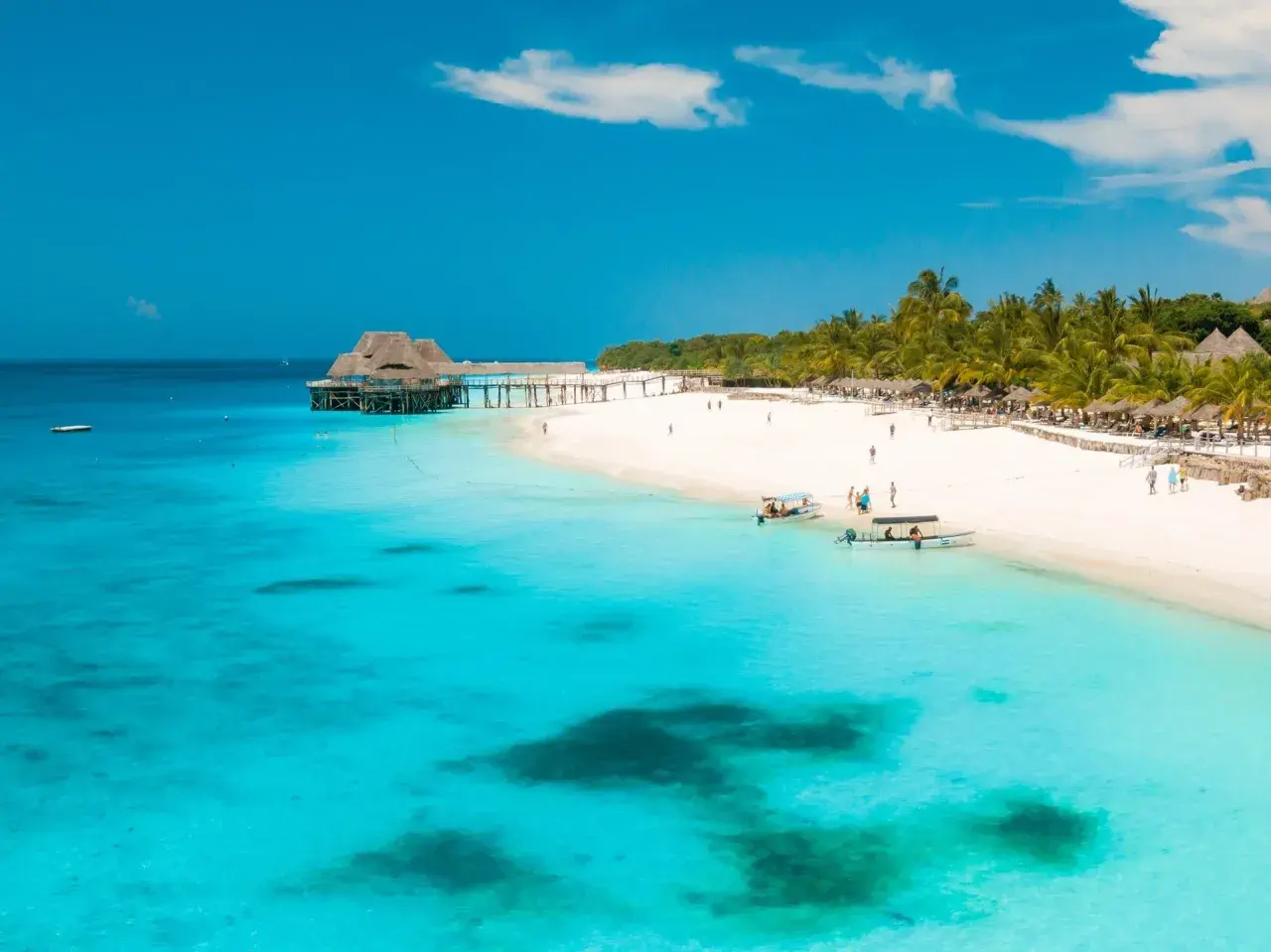 Rajskie plaże Zanzibaru w lutym. Turkusowa woda, biały piasek, palmy i urokliwy pomost z domkami na wodzie.